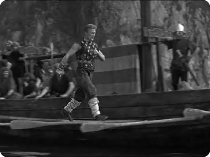 Scene from the movie "The Vikings". Kirk Douglas walks along the side of the longship, using the oars as steps. This version is cropped, and in monochrome.